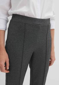 Pantalons tailored gris avec un tissu texturé, présentant une taille large et des plis avant pour une coupe structurée.