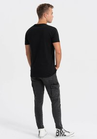 T-shirt nero a maniche corte, abbinato a pantaloni cargo grigi con tasche a patch e sneakers alte bianche con scritte nere.