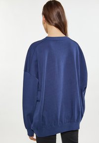 Felpa oversize blu navy con scollatura a costine e polsini, tessuto testurizzato e spalle cadute, vista dal retro.