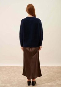 Granatowy sweter o luźnym kroju, zestawiony z długą brązową satynową spódnicą, która prezentuje gładką fakturę i subtelny połysk. Buty na blokowym obcasie.