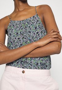 Blomster camisole med tynde stropper, der har et sort, grønt og lilla mønster. Sammen med lyserøde, stribede bukser og en rund knap.