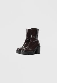 Bottines en cuir verni marron avec une semelle plateforme noire épaisse et un talon carré. Présente une finition lisse et brillante ainsi qu'une fermeture éclair sur le côté.