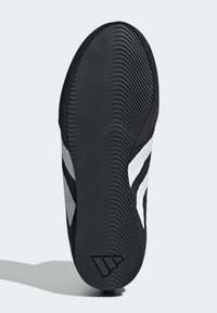 Musta urheilukengän pohja, jossa näkyvät poikittaiset syvät uurteet, valkoisia raitoja sivussa ja teksturoitu musta yläosa, joka tarjoaa pitoa.