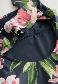 Blommönstrad tyg med rosa magnolia och gröna blad på en mörk marinblå bakgrund. Volangkrage och mjuk textur.