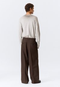 Chemise gris clair à manches longues et pantalon marron à jambes larges. La chemise présente une texture subtile, tandis que le pantalon comporte des poches arrière avec boutons.