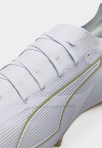 Λευκή τάπα με υφή επιφάνειας, λευκά κορδόνια και χρυσή γραμμή διακόσμησης κατά μήκος της πλευράς, σε κοντινή γωνία θέασης.