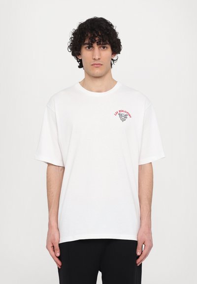 T-shirt en coton blanc à manches courtes, avec un graphisme et un texte rouge brodés sur la zone gauche de la poitrine. Design à coupe décontractée.