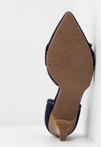 Semelle de chaussure à talon haut pointu bleu marine avec motifs de pièces en relief, marque "KAISER" et talon empilé en bois.