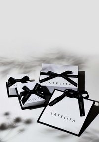 Tres cajas de regalo cuadradas en blanco con detalles en negro, que presentan cintas negras. La caja más grande está etiquetada "LATELITA."