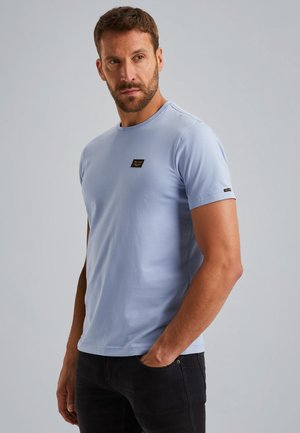 T-shirt bleu clair à manches courtes en coton avec un col rond et une petite étiquette logo noire sur la poitrine. Texture lisse.