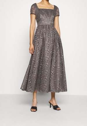 Mujer con un vestido midi de encaje gris con mangas cortas, escote cuadrado, cintura ajustada y sandalias negras de tacón con punta abierta.