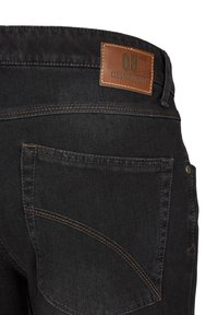 Schwarze Denim-Jeans mit einem braunen Lederetikett, auf dem "CLUB OF COMFORT" steht. Hervorstechende Nähte und Gesäßtaschen. Strukturierter Stoff.