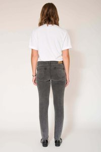 Jean skinny gris avec une taille mi-haute, une texture de tissu lisse, des poches arrière et un patch en cuir marron clair à la ceinture. Porté avec un T-shirt blanc.