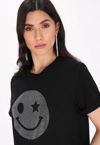 Tricou negru cu un design mare al unui smiley din cristale strălucitoare, având un ochi și o stea, cu mâneci scurte și guler rotund.