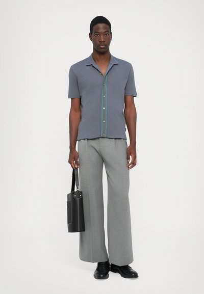Short-sleeve gray polo shirt with a green accent along the button placket, paired with light gray wide-leg trousers and a black bag.