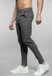 Pantalons gris ajustés avec une coupe slim, en tissu lisse, dotés de poches latérales et d'une fermeture à boutons, associés à des baskets blanches.