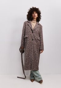 Leopardenmuster langer Mantel mit Reverskragen, zwei vorderen Taschen, Knopfverschluss, kombiniert mit hellblauen Schlagjeans und spitzen Leopardenmuster High Heels.