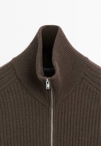 Maglione a coste marrone con colletto alto e zip argentata parzialmente chiusa, che mostra l'etichetta interna.