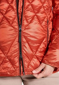 Gepolsterte, leichte Jacke in lebhaftem Rot mit einer glatten, glänzenden Oberfläche. Verfügt über einen schwarzen Reißverschluss und elastische Bündchen.