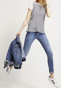 Raidoitettu, lyhythihainen paita pitsikoristeilla, yhdistettynä sinisiin slim-fit-farkkuihin ja valkoisiin tennareihin. Pitelee denimtakkiä.