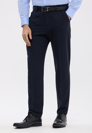 Pantaloni da dress navy con vestibilità su misura, caratterizzati da una texture liscia, tasche laterali e una cintura intrecciata nera con fibbia argentata. Indossati con scarpe nere.