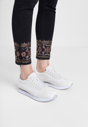 Baskets en dentelle blanche avec une tige texturée, des accents gris clair et une semelle blanche. Associez-les à un jean noir avec des broderies florales colorées.