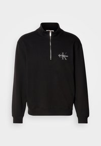 Sweat-shirt noir à manches longues avec fermeture éclair quart de zip, poignets et ourlet côtelés, avec petit logo blanc Calvin Klein sur la poitrine gauche.