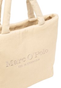 Beżowa torba typu tote z korduroy z dwoma solidnymi uchwytami, z haftowaną nazwą marki "Marc O'Polo" oraz szczegółem "EST. W SZWECJI".