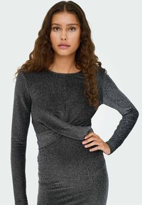 Ilgas rankovėmis pilka suknelė su blizgiu paviršiumi, priekyje esantis susukimas ir aptempianti siluetas. Lygi ir glotni medžiaga.