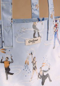 Modrý taška přes rameno z odolné látky s opakujícím se motivem cirkusových umělců, včetně hvězd a barevných akcentů. Logo Cath Kidston je viditelné.