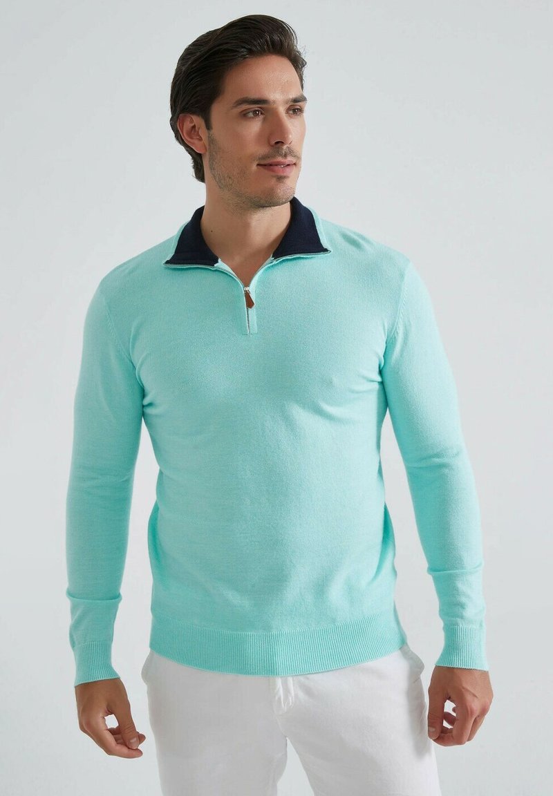 Pull léger bleu clair en tissu doux, doté d'un col navy et d'une fermeture éclair sur le devant. Manches longues avec des poignets en côte et une taille élastique.
