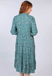 Türkises Blumenkleid mit langen Ärmeln, gerafftem Taillenbereich und gestuftem Saum. Es zeigt ein Muster aus Blumen und Blättern in Rosa und Weiß.