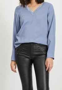 Blå V-ringad blus med spetsdetaljer, i kombination med svarta faux läderbyxor med dragkedjefickor och slim fit.