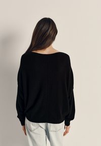 Svart oversizad tröja med bred halsringning och långa ärmar, tillverkad av ett mjukt texturerat tyg, kombinerad med ljusblå jeans.