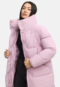 Light pink puffer coat with a high collar, featuring snap buttons and a zip closure. The fabric is smooth, with a quilted texture and a patch on the sleeve.