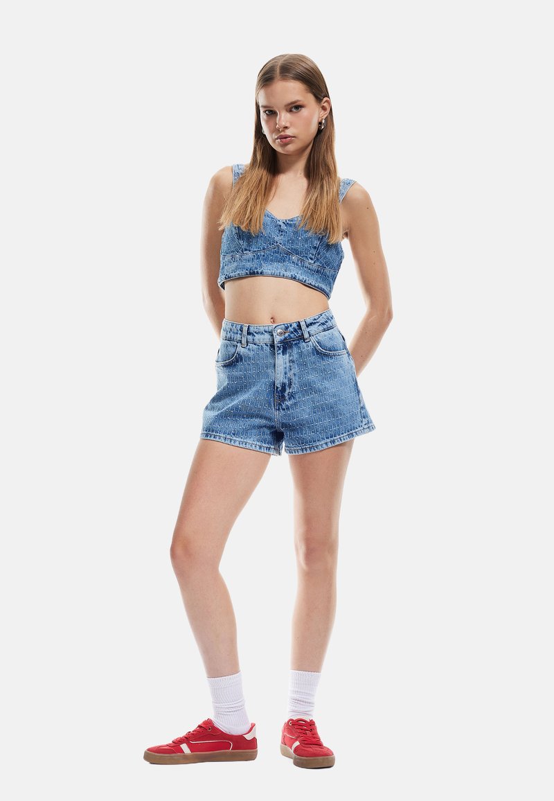 Top corto de mezclilla y pantalones cortos de tiro alto en azul claro. Presenta una textura sutil y detalles de costura. Combinado con zapatillas rojas y calcetines blancos.