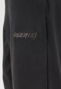 Μαύρο ύφασμα με γκρι κεντημένο κείμενο «coasted» κοντά σε ραφή σε ρούχο.