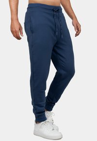 Marineblauwe joggingsbroek van zacht materiaal, met een elastische tailleband met koord, zijzakken en omgeslagen enkels.