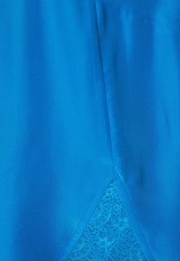 Tela de satén azul con textura suave que presenta un panel de encaje en el dobladillo, añadiendo un detalle delicado y un contraste visual.