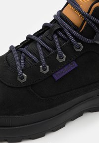 Czarne buty górskie z zamszowej cholewki, fioletowe sznurówki, metalowe oczka i zaokrąglony czubek. Wyróżniające się logo Timberland w kolorze fioletowym.