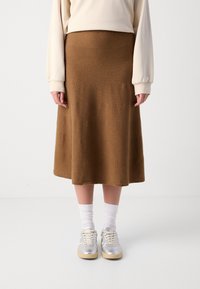 Brun, knälång ullkjol med slät textur, i kombination med grå och vita sneakers samt strukturerade vita strumpor.