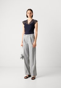Haut marin avec des manches en dentelle, design en v ; pantalon large gris clair à rayures ; sandales noires à glissière ; sac à main argenté.