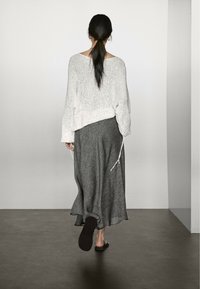 Maglione grigio chiaro a maglia con vestibilità ampia e maniche larghe, abbinato a una gonna lunga grigia scura e testurizzata, completando il look con sandali bassi.