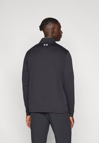 Μαύρο μακρυμάνικο μπλουζάκι με ψηλό γιακά, με μικρό λευκό λογότυπο στην πλάτη. Λείο ύφασμα με εφαρμοστή σχεδίαση.