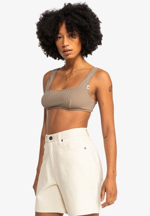 Tan ribbed bralette with wide straps, paired with high-waisted white shorts. Notable details include stitching and minimal branding.