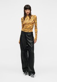 Μπλούζα με μακριά μανίκια και μοτίβο τιγρέ πορτοκαλί και μαύρου χρώματος, συνδυασμένη με μαύρο δερμάτινο παντελόνι φαρδιάς γραμμής και διαφανή παπούτσια με τακούνι.