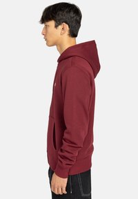 Bordeaux hoodie met een zak aan de voorkant en geribbelde manchetten, voorzien van een klein logo detail op de borst, in een zachte, gestructureerde stof.