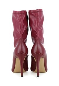 Une paire de bottines à talons hauts en cuir bordeaux avec des talons aiguilles pointus, présentée de dos sur un fond blanc.