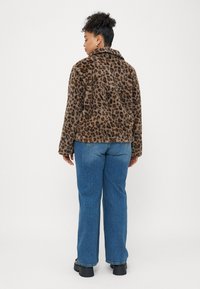 Jachetă din blană sintetică cu imprimeu leopard, cu guler, asociată cu blugi drepți albaștri deschiși și bocanci negri masivi, văzută din spate.