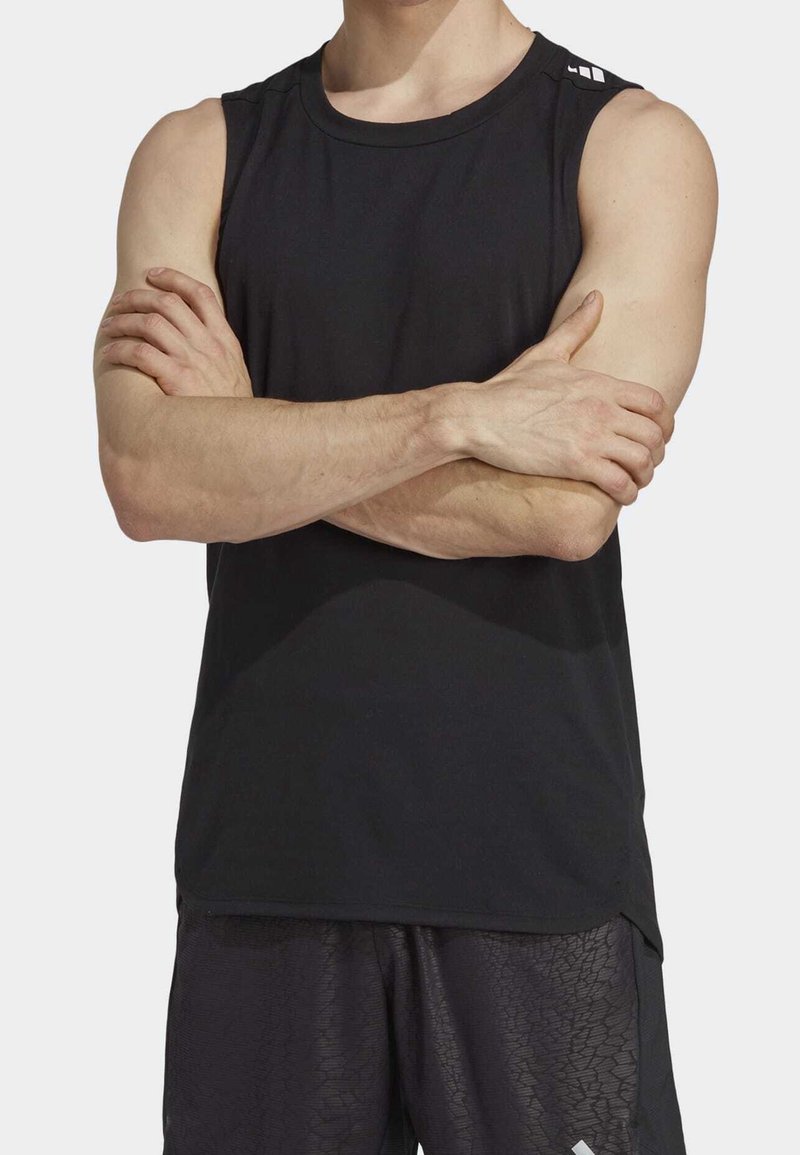 Homme portant un débardeur de sport noir et un short texturé noir, les bras croisés sur la poitrine.